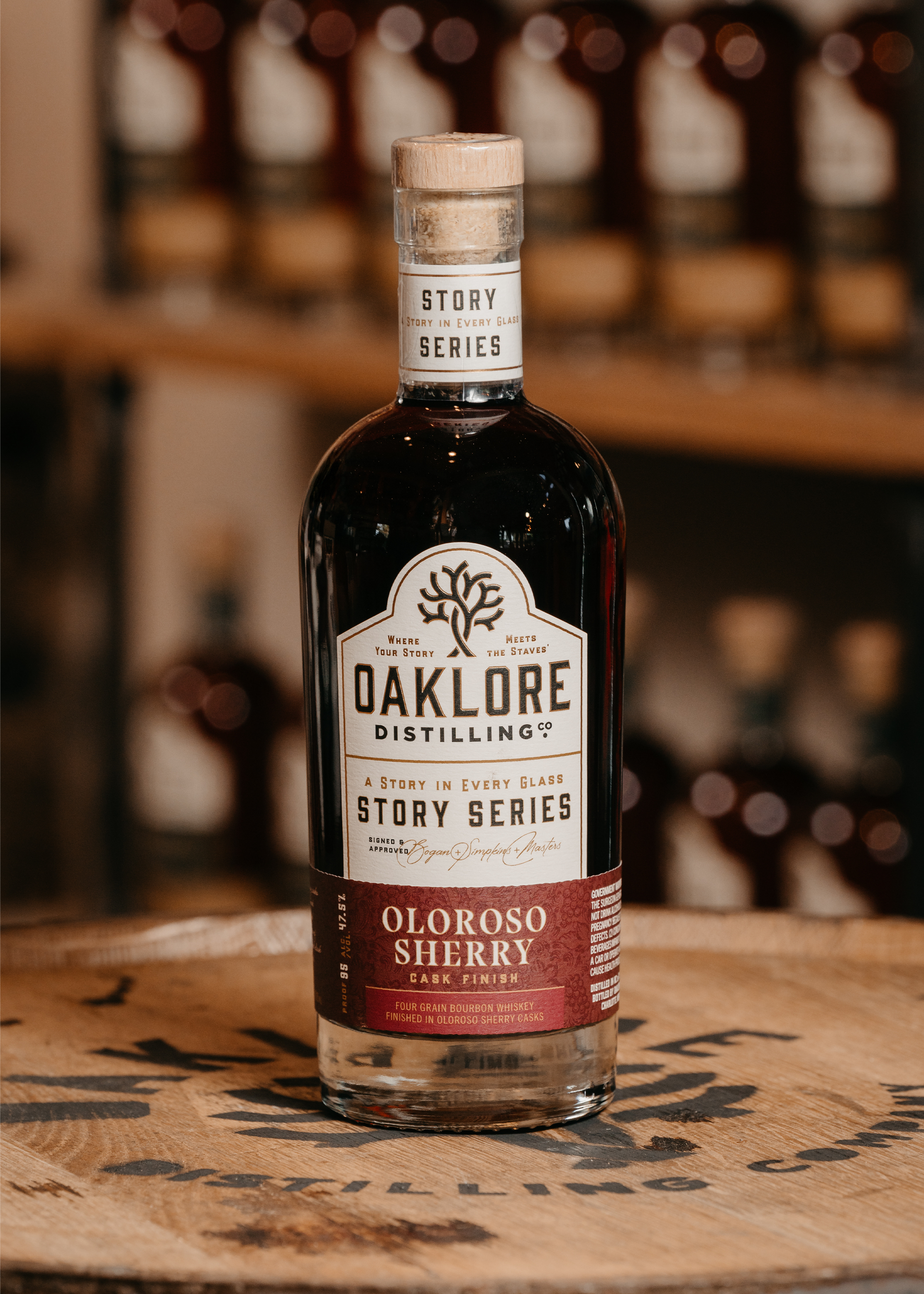 Bottle of Oaklore Distilling Oloroso Sherry on a wooden barrel with blurred bottles in the background.